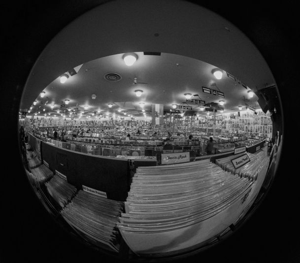 Fisheye view of an extensive record store, filled with rows of albums and bright ceiling lights, creating a wide, circular distortion.