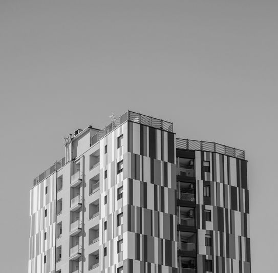 Image en noir et blanc d’un immeuble de grande hauteur aux motifs rayés verticaux, se détachant sur un ciel dégagé.