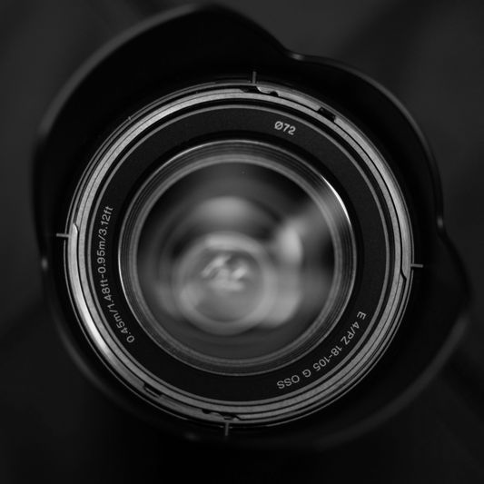 Primer plano de una lente de cámara con anillos de apertura y marcas visibles, sobre un fondo oscuro.