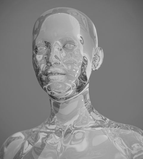 Une sculpture humanoïde transparente et réfléchissante avec des traits du visage détaillés, sur un fond gris neutre.