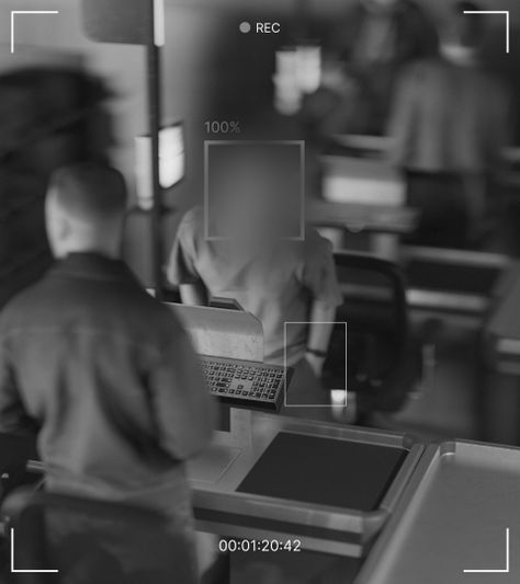 Surveillance camera view of a person at a self-checkout counter in a store. Display screens and a keypad are visible.
