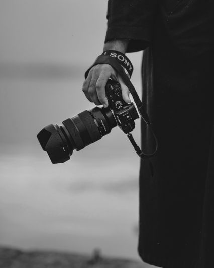 Personne tenant un appareil photo Sony avec un grand objectif, vêtue d'un manteau sombre, debout à l'extérieur dans un environnement brumeux.