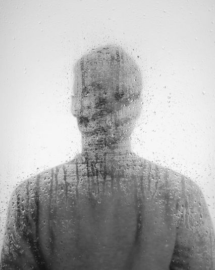 Silhouette of a person behind a rain-soaked, foggy glass, creating a blurred and mysterious effect.