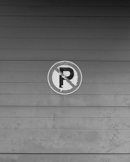 Imagen en blanco y negro de un cartel de "No estacionar" en una pared de madera con paneles horizontales.