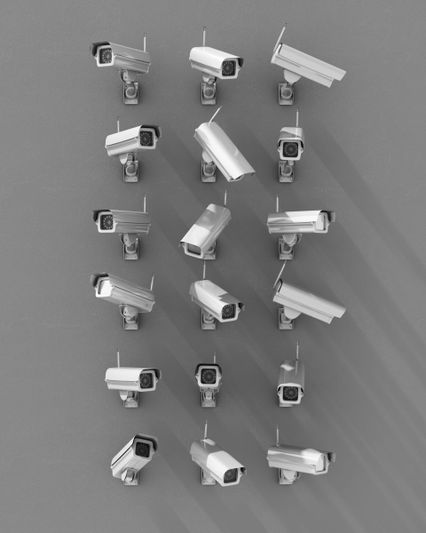 Rows of various security cameras mounted on a gray wall, casting long shadows.