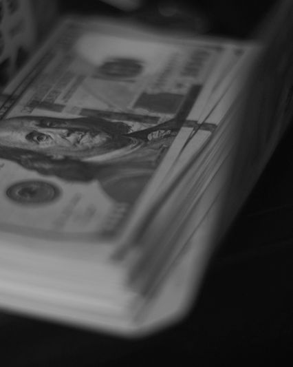 Une pince en métal maintient une pile de billets en dollars américains et en euros sur un simple fond gris.