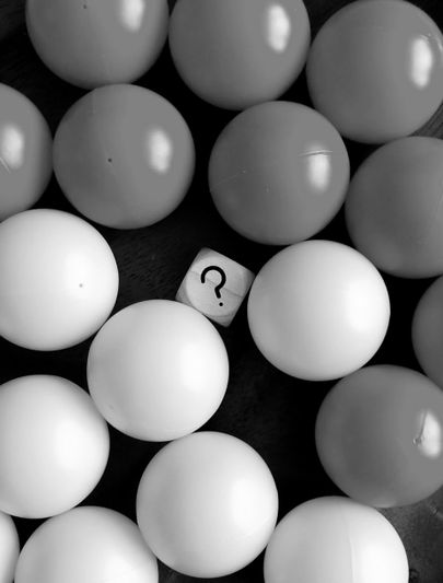 Imagen en blanco y negro de un grupo de bolas redondas con un dado en el centro que muestra un signo de interrogación.