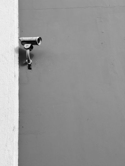 Image en noir et blanc d'une caméra de sécurité fixée au mur, tournée vers la gauche. Le mur est divisé en une partie claire et une partie sombre.