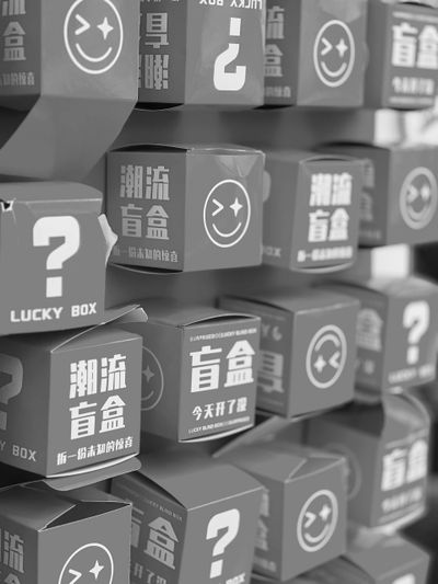Stacked lucky boxes with question marks and winking smiley faces, inscribed with Japanese text, displayed on shelves.