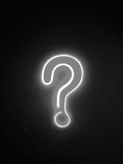 Glowing white neon question mark sign mounted on a dark textured wall.