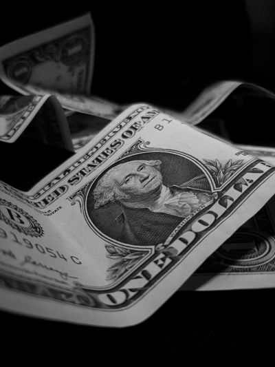 Gros plan de billets de dollar américains froissés en noir et blanc, mettant en avant un billet d'un dollar en premier plan.