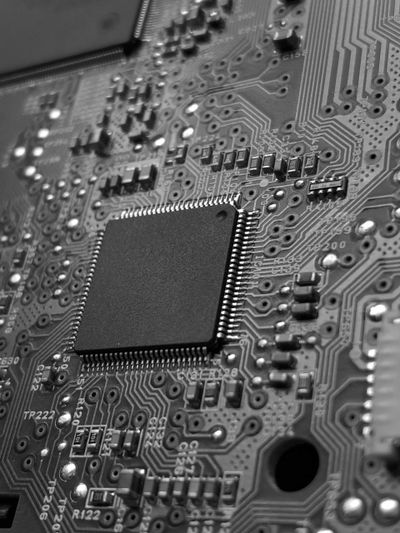 Primer plano de una placa base de computadora en blanco y negro, con un chip de circuito integrado rodeado de un intrincado circuito y componentes.