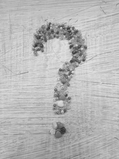 Un point d'interrogation composé de petites perles disposées sur une surface en bois rayée.