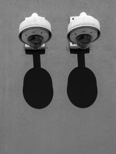 Deux caméras de sécurité montées sur un mur, projetant des ombres ovales distinctes en dessous d'elles en plein soleil.
