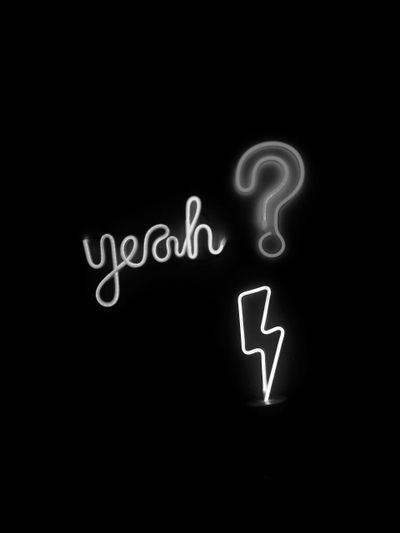 Neon signs against a black background depicting the word "yeah," a question mark, and a lightning bolt.