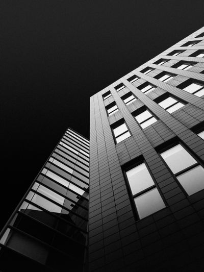 Vue en contre-plongée de deux bâtiments modernes aux fenêtres en grille, se détachant sur un ciel sombre, mettant en valeur la netteté de leurs lignes et leur conception géométrique.