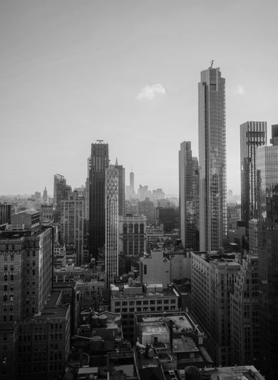 Paysage urbain en noir et blanc de hauts gratte-ciel sous un ciel clair, avec une vue lointaine d'une tour en arrière-plan.