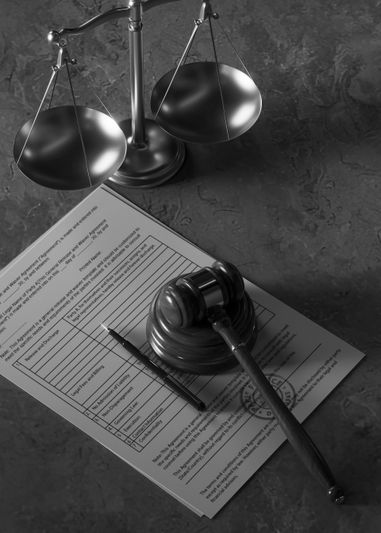 Un marteau et un stylo reposent sur des documents juridiques sous une balance de la justice sur une surface texturée sombre.