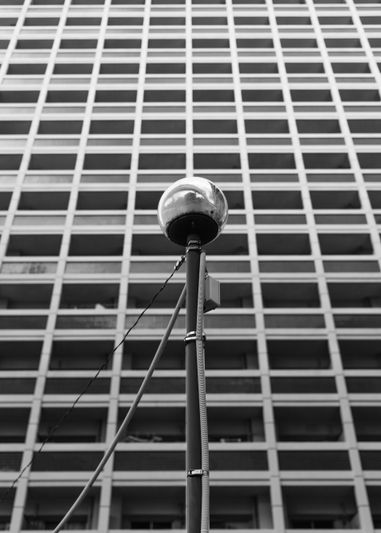 Una foto en blanco y negro de una farola esférica frente a un edificio alto con un patrón de ventanas y balcones en forma de cuadrícula.