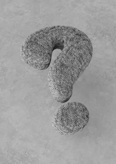 A three-dimensional, fluffy question mark on a textured gray surface, casting a soft shadow.