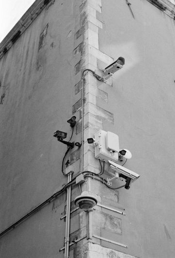 Una esquina de un edificio con múltiples cámaras de seguridad y cableado, capturada en blanco y negro.
