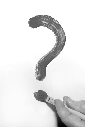 Signo de interrogación negro pintado con un pincel sobre fondo blanco. En la parte inferior se ve una mano sosteniendo un pincel.