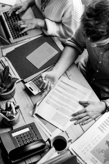 Deux personnes travaillent à un bureau avec un ordinateur portable, des documents, une calculatrice et des fournitures de bureau, vues d'en haut.