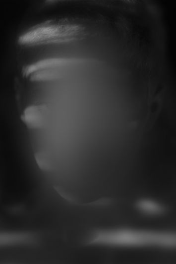 Una imagen borrosa y monocromática de un rostro con patrones de luz y sombra que ocultan los rasgos, creando un efecto misterioso.