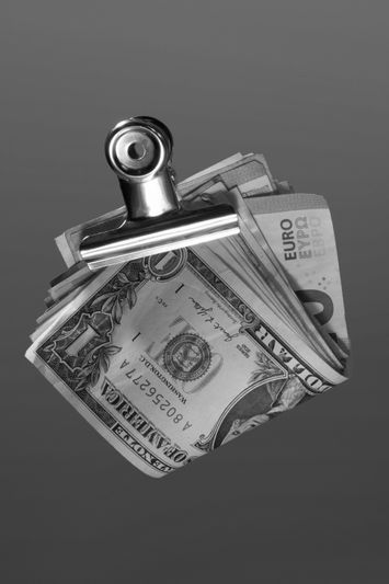 Une pince en métal maintient une pile de billets en dollars américains et en euros sur un simple fond gris.