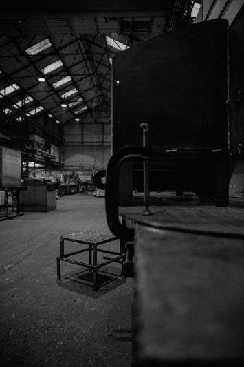 Fotografía en blanco y negro del interior vacío de un gran almacén industrial con techos altos y equipos dispersos.