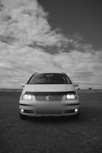 black-and-white photo of the front of a white Volkswagen car with a blurred license plate
