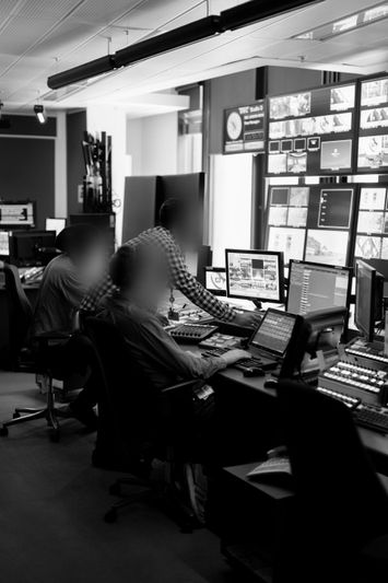 Leute, die in einem Kontrollraum arbeiten, nutzen mehrere Bildschirme und elektronische Geräte und konzentrieren sich darauf, verschiedene digitale Anzeigen zu überwachen.