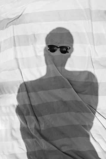 Sombra de una persona usando gafas de sol sobre un fondo de tela a rayas, creando un efecto abstracto y artístico.