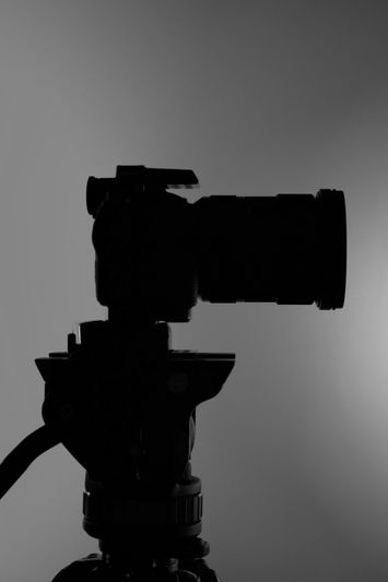 Silueta de una cámara en un trípode contra un fondo gris.