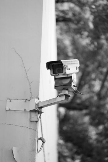 cámara de vigilancia blanca de modelo antiguo sujeta a la pared de un edificio con árboles de fondo