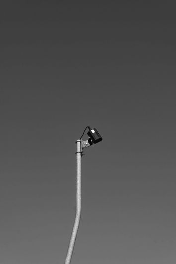 Un seul lampadaire contre un ciel clair et sombre, capturé en noir et blanc, avec le luminaire légèrement incliné vers le haut.