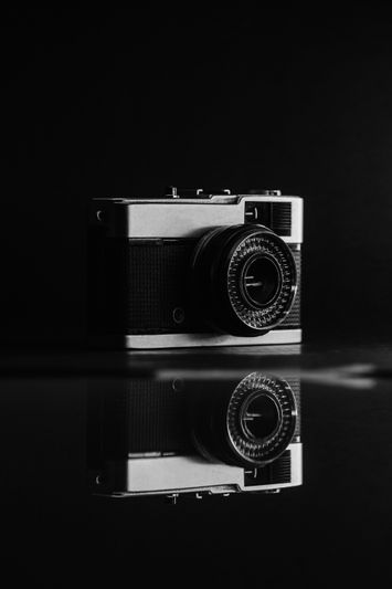 Una cámara antigua se encuentra sobre un fondo oscuro, y su reflejo es visible en la superficie brillante que hay debajo.