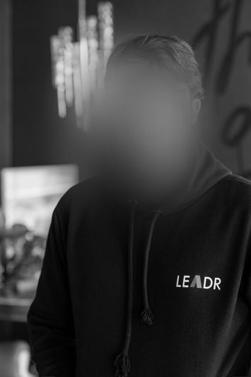 black-and-white photo of a woman with a blurred animated face wearing a black hoodie with the word 'leadr'
