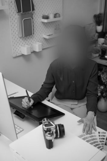 Personne utilisant une tablette graphique à un bureau avec un appareil photo, des nuanciers de couleurs et un ordinateur, dans un espace de travail créatif. Les visages sont intentionnellement floutés.