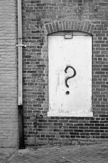 Un mur en briques montre une fenêtre repeinte avec un grand point d'interrogation noir dessus. Un tuyau court verticalement à côté de la fenêtre.