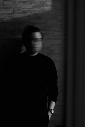 Silueta borrosa de una persona con ropa oscura apoyada contra una pared texturizada, con la luz proyectando sombras.