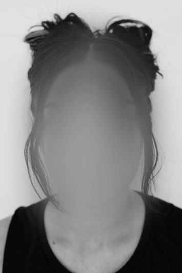 Schwarz-Weiß-Foto einer Frau mit braunen Haaren und einer Halskette, deren Gesicht unscharf ist