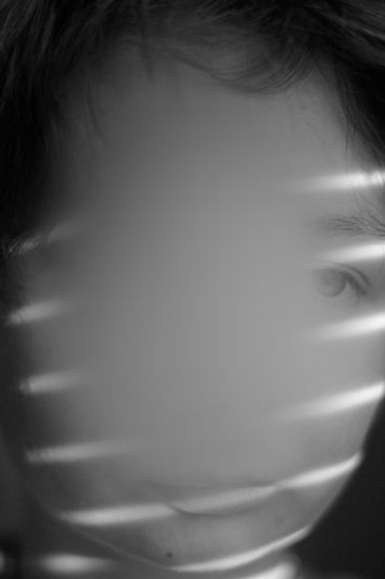 A person's face partially obscured by a blurred effect, with striped light patterns across the face in black and white.