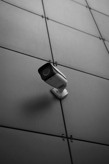A security camera mounted on a modern, dark tiled wall, angled slightly downward.