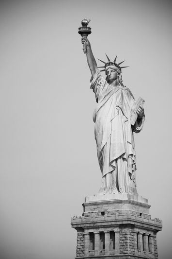 Image en noir et blanc de la Statue de la Liberté, tenant une torche et une tablette, contre un ciel clair.