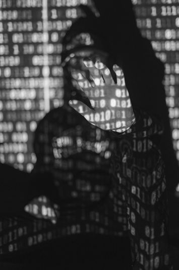 Person with hand raised, obscured by shadow and illuminated by binary code projections in black and white.