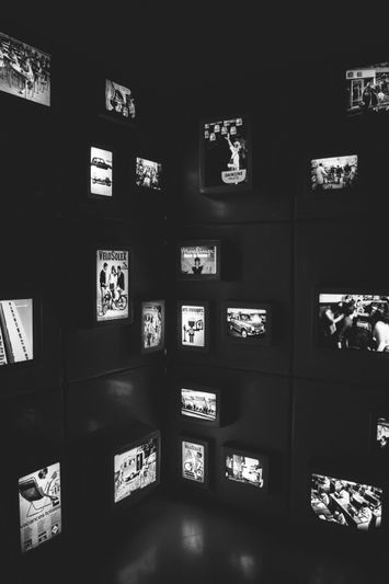 Une pièce faiblement éclairée avec plusieurs écrans affichant des images et des publicités vintage en noir et blanc sur des murs sombres.