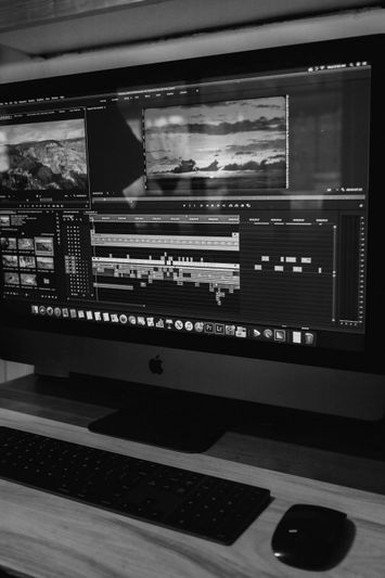 Computer screen displaying video editing software with timelines and clips, on a desk with a keyboard and mouse.