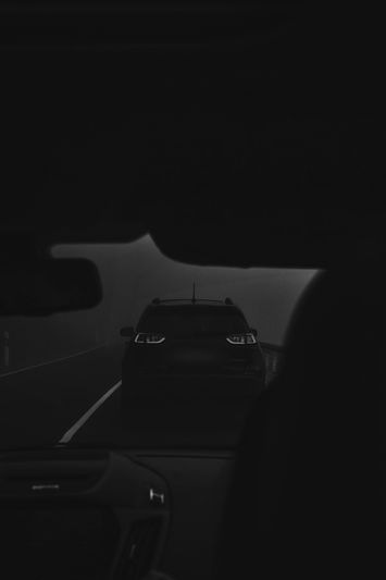 Dark, foggy road view from inside a car, focusing on the rear of another vehicle with illuminated taillights ahead.