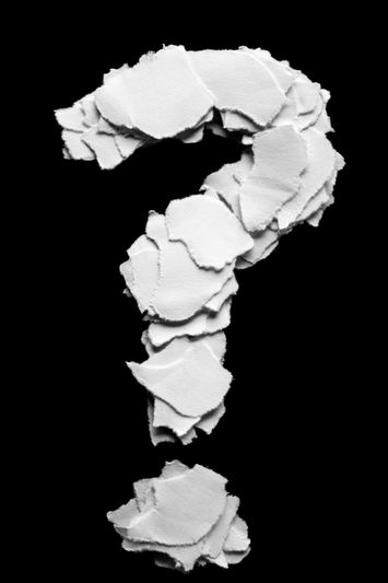 Un signo de interrogación hecho de pedazos de papel blanco rasgado colocados sobre un fondo negro.